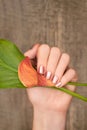 Beautiful female hand with pink nail design holding calla lily. Female hand with glitter manicure on wooden background Royalty Free Stock Photo