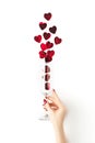 Beautiful female hand with trendy red manicure holding champagne glass with vibrant red heart-shaped confetti poured out