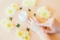 Beautiful female hands and cosmetic cream and yellow flowers on a beige background. To smear arms or hand with a cream, an elastic