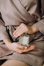 Beautiful female hands hold a glass bottle of perfume. Delicate morning preparation in a beige silk dressing gown Royalty Free Stock Photo