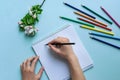 Beautiful female hands hold a pencil over a notebook. On a blue background, colored pencils, the concept of creativity and drawing Royalty Free Stock Photo