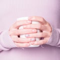 Beautiful female hands holding white cup on the pale violet background. Manicure with pink color nail polish with shiny design.
