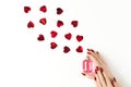 Beautiful female hands with trendy red manicure holding stylish bottle of perfume with spray of vibrant red heart-shaped