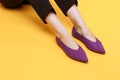 Beautiful female legs are dressed in stylish violet flat shoes. violet sandals on a yellow background Royalty Free Stock Photo