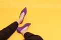 Beautiful female legs are dressed in stylish violet flat shoes. violet sandals on a yellow background Royalty Free Stock Photo