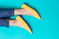 Beautiful female legs are dressed in stylish yellow shoes without a heel. Light yellow summer sandals on a blue background Royalty Free Stock Photo