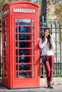 Attractive Lonodn traveler woman stands next to a classic, red telephone booth Royalty Free Stock Photo