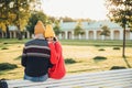 Beautiful female in loose red sweater embraces her boyfriend, missed him too much as didn`t see long ago, sit on bench in park, ha Royalty Free Stock Photo