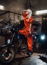 Beautiful female mechanic in orange overalls hold a big wrench and posing for a camera in garage Royalty Free Stock Photo