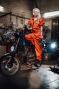Beautiful female mechanic in orange overalls hold a big wrench and posing for a camera in garage Royalty Free Stock Photo