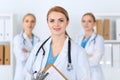 Beautiful female medical doctor standing at hospital in front of medical group. Physician is ready to help patients