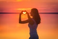 Beautiful female model enjoying sunset and making heart sign on sun. Calm water of salt lake Elton reflects woman`s silhouette. Gi Royalty Free Stock Photo