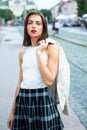 Beautiful female model hold the white suit across sholder in summer city in Europe. Trendy woman posing on the street