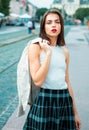 Beautiful female model hold the white suit across sholder in summer city in Europe. Trendy woman posing on the street