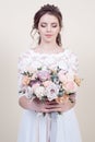 Beautiful female model holding a bouquet of flowers wearing in luxurious long lacy dress isolated on background