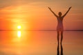 Beautiful female model open arms under sunrise at seaside. Calm water of salt lake Elton reflects woman silhouette. Sun goes Royalty Free Stock Photo