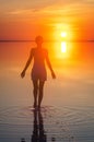 Beautiful female model open arms under sunrise at seaside. Calm water of salt lake Elton reflects woman silhouette. Sun goes Royalty Free Stock Photo