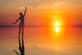 Beautiful female model open arms under sunrise at seaside. Calm water of salt lake Elton reflects woman silhouette. Sun goes Royalty Free Stock Photo