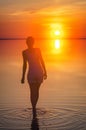 Beautiful female model open arms under sunrise at seaside. Calm water of salt lake Elton reflects woman silhouette. Sun goes Royalty Free Stock Photo