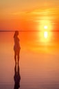 Beautiful female model open arms under sunrise at seaside. Calm water of salt lake Elton reflects woman silhouette. Sun goes Royalty Free Stock Photo