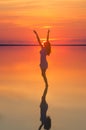 Beautiful female model open arms under sunset at seaside. Calm water of salt lake Elton reflects woman silhouette. Sun goes behind Royalty Free Stock Photo