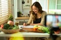 Beautiful female nutritionist sitting at desk and writing diet plan, recording video content on smartphone Royalty Free Stock Photo