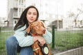 Beautiful female owner hugs a cute brown breed dog magyar vizsla and looks into the camera, sitting on a walk. Owner loves his dog