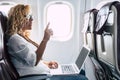 Beautiful female passeger of airplane use personal laptop computer on board with wifi internet connection and ask for hostess help