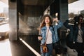 Beautiful female photographer in trendy outfit with black phone posing smiling near shopping center. Portrait of