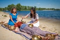 Beautiful female receiving energy sound massage with singing bowls and body massage on a river bank