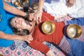 Beautiful female receiving energy sound massage with singing bowls and body massage on a river bank