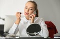 Beautiful female secretary applying makeup while talking on mobile phone in office Royalty Free Stock Photo