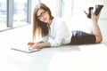 Beautiful female specialist with laptop computer laying on the floor in modern office and smiling charmingly. Working on