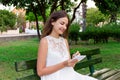 Beautiful female student is writing her ideas and thoughts into the notebook sitting on the bench in the park