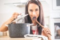 Beautiful female tasting from a wooden spoon, holding lid open above the pot, smiling into the camera Royalty Free Stock Photo