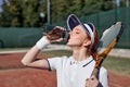 Beautiful female tennis player on hardcourt, having rest, drinking fresh water Royalty Free Stock Photo