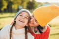 Beautiful female in yellow knitted hat kisses her adorable little child, have wonderful unforgettable time together. Small child s