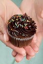 Beautiful feminine hand holding tasty appetizing chocolate cupcake. Blue Background. Closeup.