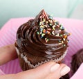 Beautiful feminine hand holding tasty appetizing chocolate cupcake. Pink Gift Box. Closeup.