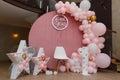Beautiful festive decorations, pink and golden balloons arch, wooden stars, white chair and number one on wooden round background