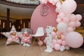 Beautiful festive decorations, pink and golden balloons arch, wooden stars, white chair and number one on wooden round background