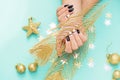 Beautiful festive female manicure. Women`s hands hold a small gift. New Year`s content, balls, sequins, stars