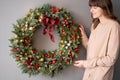 Beautiful festive wreath of fresh spruce in woman hands. Xmas circlet with red and gold ornaments and balls. Christmas Royalty Free Stock Photo