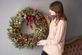 Beautiful festive wreath of fresh spruce in woman hands. Xmas circlet with red and gold ornaments and balls. Christmas Royalty Free Stock Photo