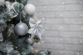 Beautiful fir tree decorated with white baubles and silver bows on brick wall with golden garland lights bokeh. Merry Christmas. Royalty Free Stock Photo
