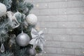 Beautiful fir tree decorated with white baubles and silver bows on brick wall with golden garland lights bokeh. Merry Christmas. Royalty Free Stock Photo