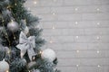 Beautiful fir tree decorated with white baubles and silver bows on brick wall with golden garland lights bokeh. Merry Christmas. Royalty Free Stock Photo