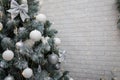 Beautiful fir tree decorated with white baubles and silver bows on brick wall with golden garland lights bokeh. Merry Christmas. Royalty Free Stock Photo