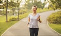 Beautiful fit blonde woman running at the park on a sunny day. Young Female runner listening to music while jogging Royalty Free Stock Photo