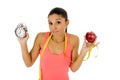 Beautiful and fit hispanic woman holding alarm clock apple fruit and taylor measure tape Royalty Free Stock Photo